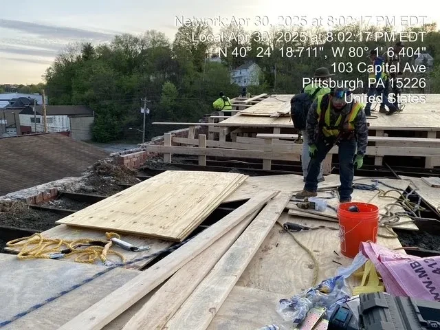 Crew working on exposed roof framing with generator and tools at 1828 W Liberty Ave