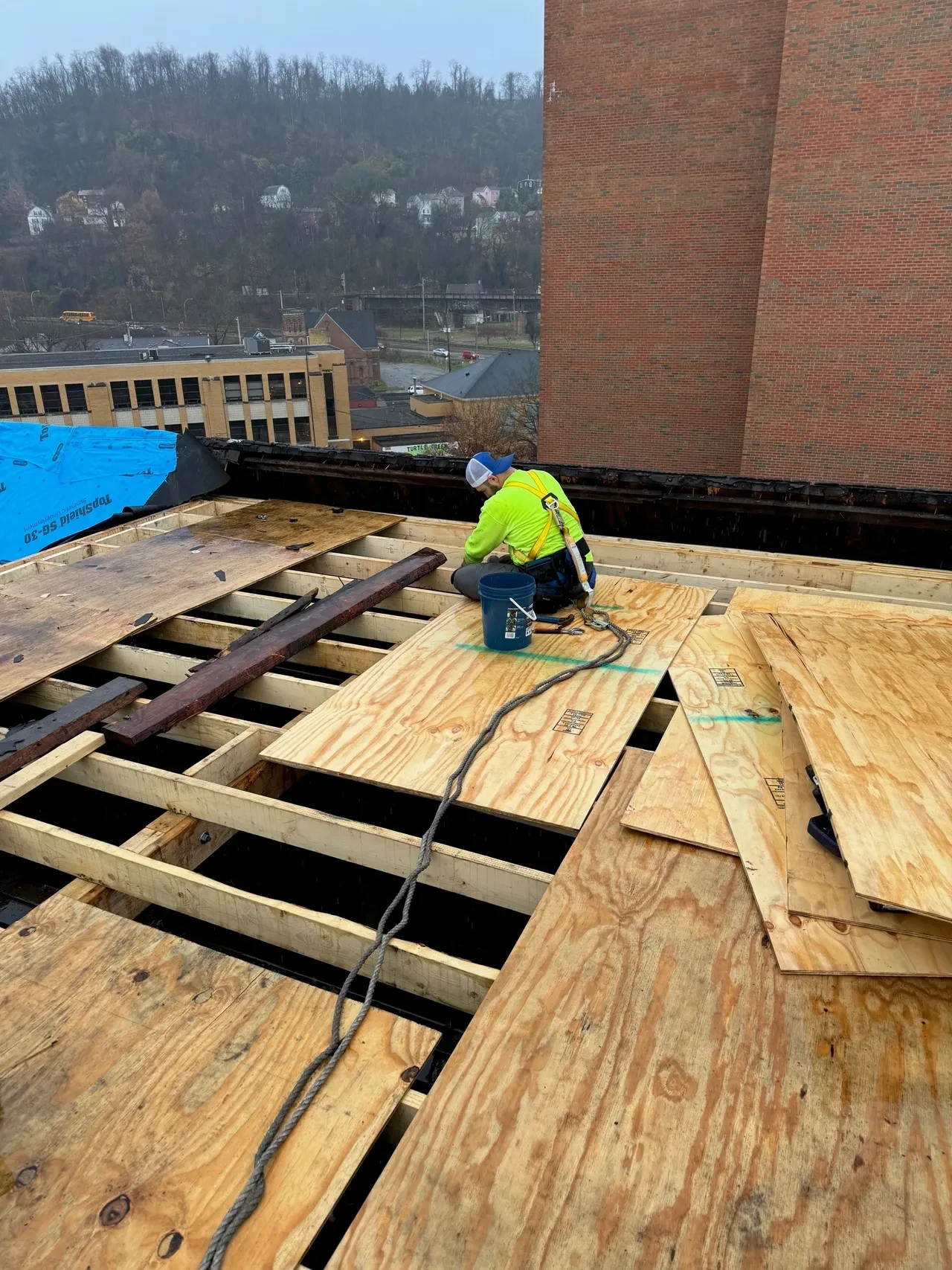 Active rooftop worksite on government building with yellow safety perimeter guards, lumber, and tools staged across the deck