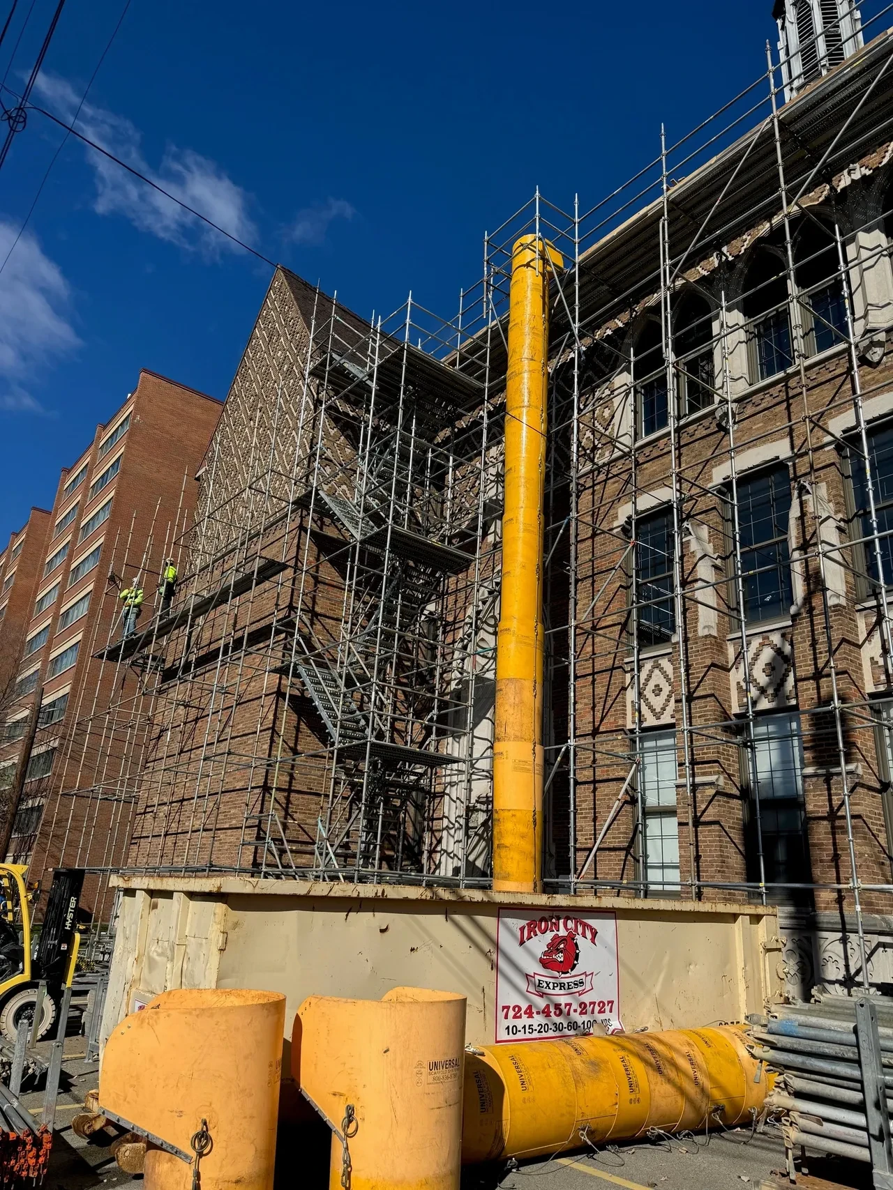 Worker in harness installing new plywood decking over exposed roof framing on government building